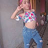 casual_clothing, child, curly_hair, denim_jeans, floor_tiles, floral_top, flowers, girl, hallway, headband, indoor, peace_sign, person, pink_boots, playful, portrait, posing, smiling, vase, wall