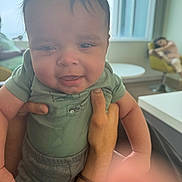 Zayvion joined the competition — help win amazing prizes! baby, child, hands, indoor, smiling, person, window, chair, furniture, table, green_clothing, adult_hand, modern_interior, blurred_background, relaxed, portrait, happy, casual, short_hair, daylight