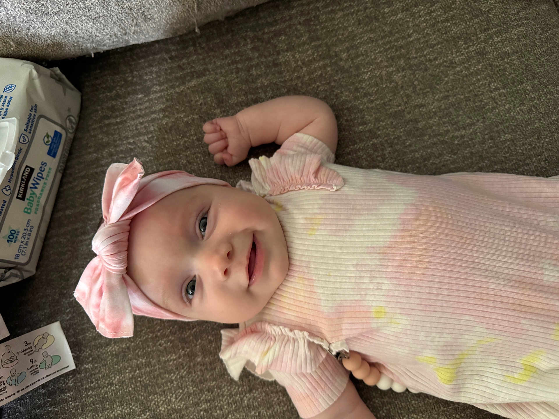 Carter is registered to the contest to win money with this photo: baby, infant, smile, headband, pink, ribbon, carpet, floor, baby_wipes, clothing, pastel_colors, cute, child, portrait, lying_down, happy, small_arm, indoor, soft_texture, rippled_fabric
