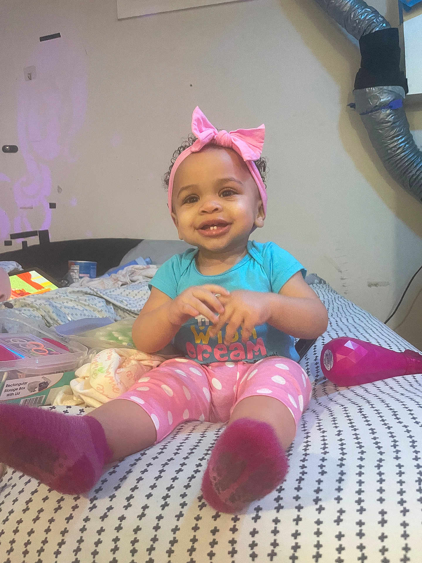 Raeven is registered to the contest to win money with this photo: toddler, child, smiling, pink_bow, headband, polka_dot_pants, socks, bed, room, ventilation_duct, toys, storage_box, blanket, happy, indoor, person, clothing, pattern, furniture, baby