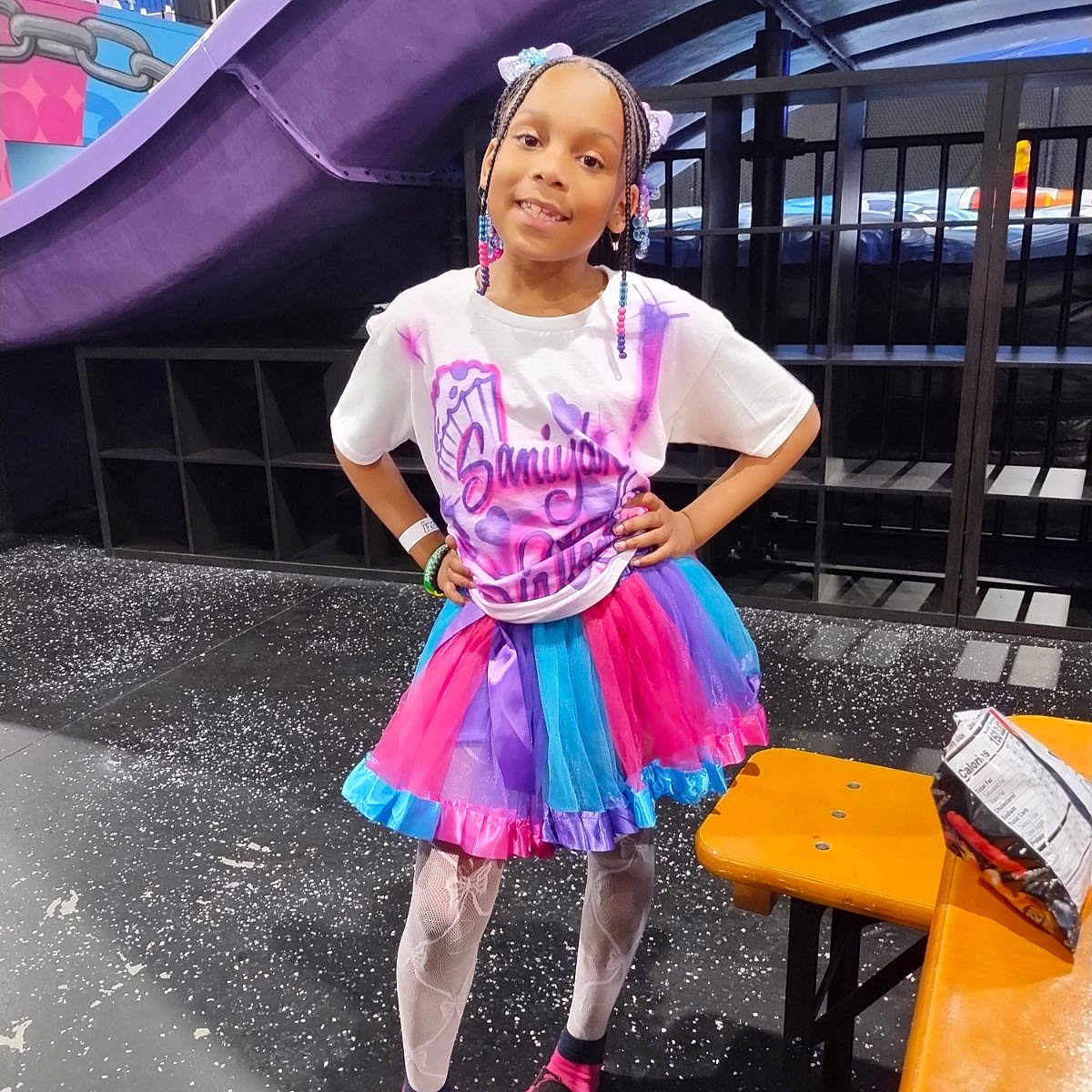 Saniyah is registered to the contest to win money with this photo: child, clothing, face, female, footwear, girl, hair, head, person, photography, portrait, purple, sandal, shoe, sitting, skirt, sleeve, standing, student, t_shirt