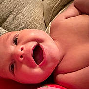 Josie joined the competition — help win amazing prizes! baby, infant, smiling, face, skin, mouth, eyes, couch, cushion, texture, happy, lying_down, closeup, indoors, child, person, expression, warm_lighting, portrait, bare_skin