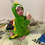 Medine participe au concours pour gagner de l'argent avec cette photo : baby, bed, blanket, child, cozy, curious, cute, dinosaur_onesie, foot, giraffe_print, green_costume, indoor, jungle_theme, playful, plush_toy, sitting, smiling, soft_toys, toddler, wall