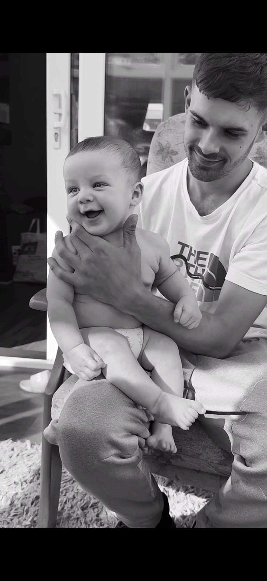 Oakley is registered to the contest to win money with this photo: baby, child, man, smile, happy, indoor, black_and_white, affection, holding, seated, diaper, casual_clothing, young_adult, joy, parenting, love, face, portrait, home, bonding