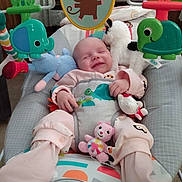 Violet is registered to the contest to win money with this photo: baby, smiling, infant, baby_bouncer, toy, stuffed_animal, elephant_toy, frog_toy, monkey_image, turtle_toy, pink_pajamas, comfort, indoor, child, cute, happy, playtime, soft_toys, seat, relaxed