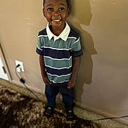 Gaberial is registered to the contest to win money with this photo: child, boy, smiling, indoor, striped_shirt, polo_shirt, dark_pants, carpet, wall, shadow, happy, standing, home, electric_socket, footwear, portrait, casual_clothing, cute, young, person