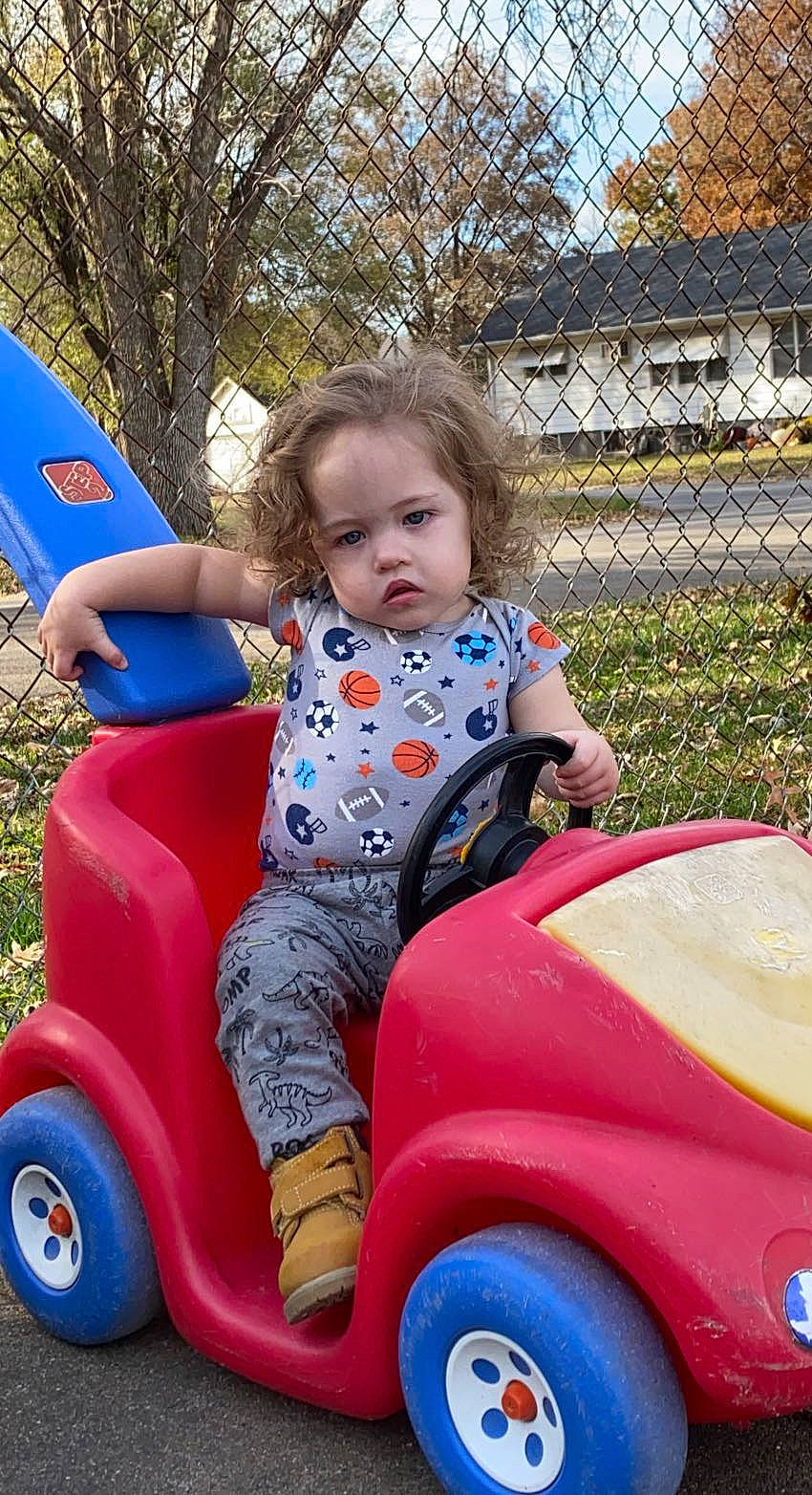 Elliot is registered to the contest to win money with this photo: automotive_tire, baby, baby_toddler_clothing, child, fender, fun, grass, happy, leisure, motor_vehicle, person, photograph, pink, plant, recreation, riding_toy, tire, toddler, tree, vehicle