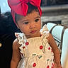 toddler, child, red_bow, headband, white_dress, cherry_print, indoor, portrait, cute, curious, person, fashion, clothing, sitting, young_child, face, skin, hair, earrings, accessory