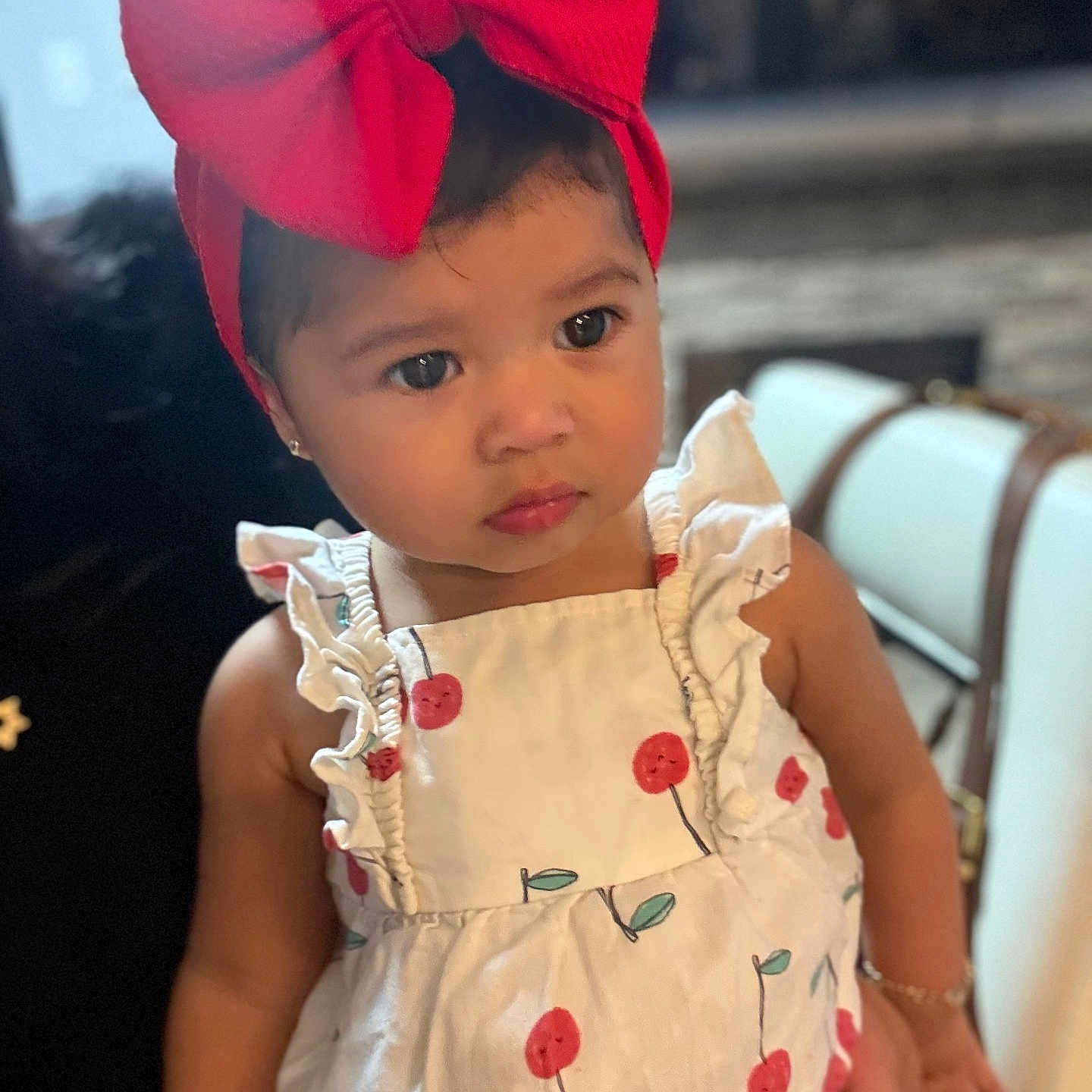 Aleah Arambula joined the competition — help win amazing prizes! toddler, child, red_bow, headband, white_dress, cherry_print, indoor, portrait, cute, curious, person, fashion, clothing, sitting, young_child, face, skin, hair, earrings, accessory