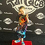child, smiling, peace_sign, red_carpet, colorful_clothing, backdrop, logo, hashtag, event, footwear, standing, pose, fun, indoor, person, happy, shorts, tshirt, blue_shoes, carpet