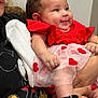 adult, affection, baby, black_shirt, cartoon_character, child, chubby_cheeks, curly_hair, cute, glasses, hands, happy, heart_pattern, holding, indoor, person, portrait, red_dress, smiling, socks