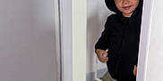 Waylon participe au concours pour gagner de l'argent avec cette photo : child, kid, hoodie, black_hoodie, smile, indoor, doorway, peek, sneaky, casual_clothing, sneakers, floor, wood_floor, candid, portrait, person, young, cute, playful, home
