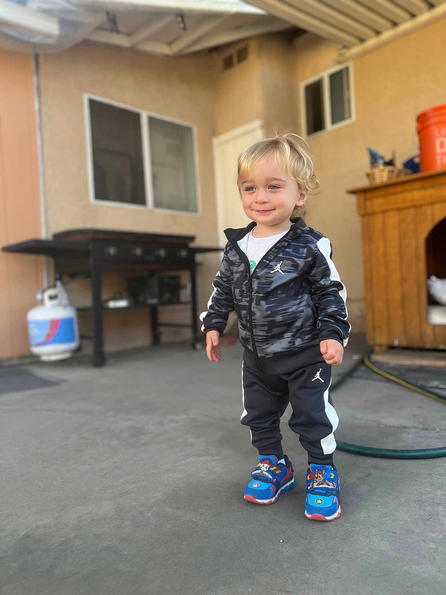 Atom joined the competition — help win amazing prizes! toddler, child, boy, smiling, standing, tracksuit, sneakers, outdoor, patio, concrete, propane_tank, grill, doghouse, window, hose, building, casual, daylight, cute, happy