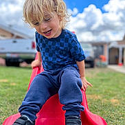 Atom joined the competition — help win amazing prizes! child, blonde_hair, blue_shirt, navy_pants, black_shoes, red_slide, grass, outdoor, playground, smiling, happy, cloudy_sky, daytime, backyard, person, casual_clothing, fun, leisure, young_child, curly_hair