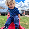child, blonde_hair, blue_shirt, navy_pants, black_shoes, red_slide, grass, outdoor, playground, smiling, happy, cloudy_sky, daytime, backyard, person, casual_clothing, fun, leisure, young_child, curly_hair