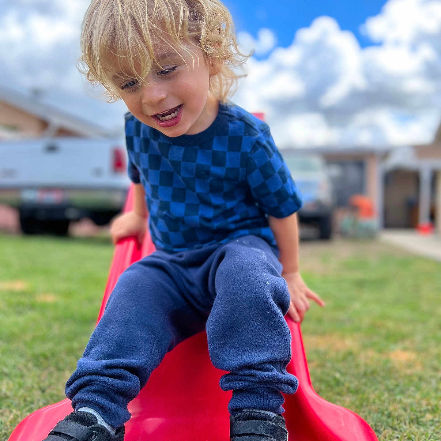Atom joined the competition — help win amazing prizes! child, blonde_hair, blue_shirt, navy_pants, black_shoes, red_slide, grass, outdoor, playground, smiling, happy, cloudy_sky, daytime, backyard, person, casual_clothing, fun, leisure, young_child, curly_hair