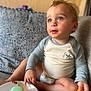 blue_eyes, candid, casual, child, couch, curious, curly_hair, diaper, food, indoor, light, long_sleeve_shirt, messy_face, patterned_cushion, pointing, portrait, sitting, snack_container, toddler, young_child
