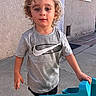 blonde, blue_toy, casual_clothing, child, concrete, curly_hair, door, expression, grey_tshirt, nike_logo, outdoor, person, playtime, portrait, sidewalk, summer, sunlight, toy_truck, wall, young_child