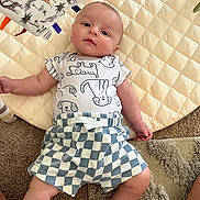 Angel joined the competition — help win amazing prizes! baby, infant, child, onesie, shorts, plaid, quilted_mat, carpet, toy, animal_print, cute, lying_down, indoor, soft_texture, playtime, curious, person, skin, face, legs