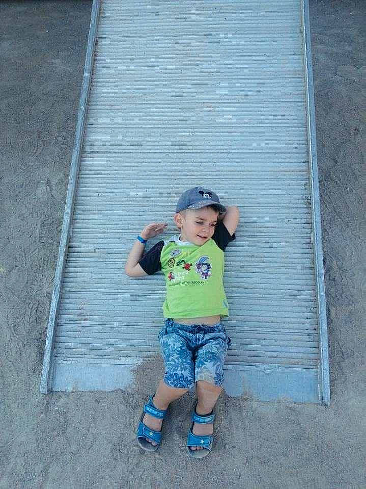 Louis a rejoint le concours — aidez-le/la à gagner de superbes lots ! asphalt, baby_toddler_clothing, child, concrete, denim, electric_blue, grass, hat, headwear, human_leg, leisure, pattern, person, road, road_surface, sandal, shadow, shorts, sidewalk, sitting