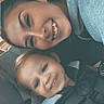 woman, toddler, car_seat, smile, happy, child, person, safety_harness, seatbelt, braid, casual_clothing, indoor, closeup, portrait, family, car_interior, child_safety, bonding, joy, transportation