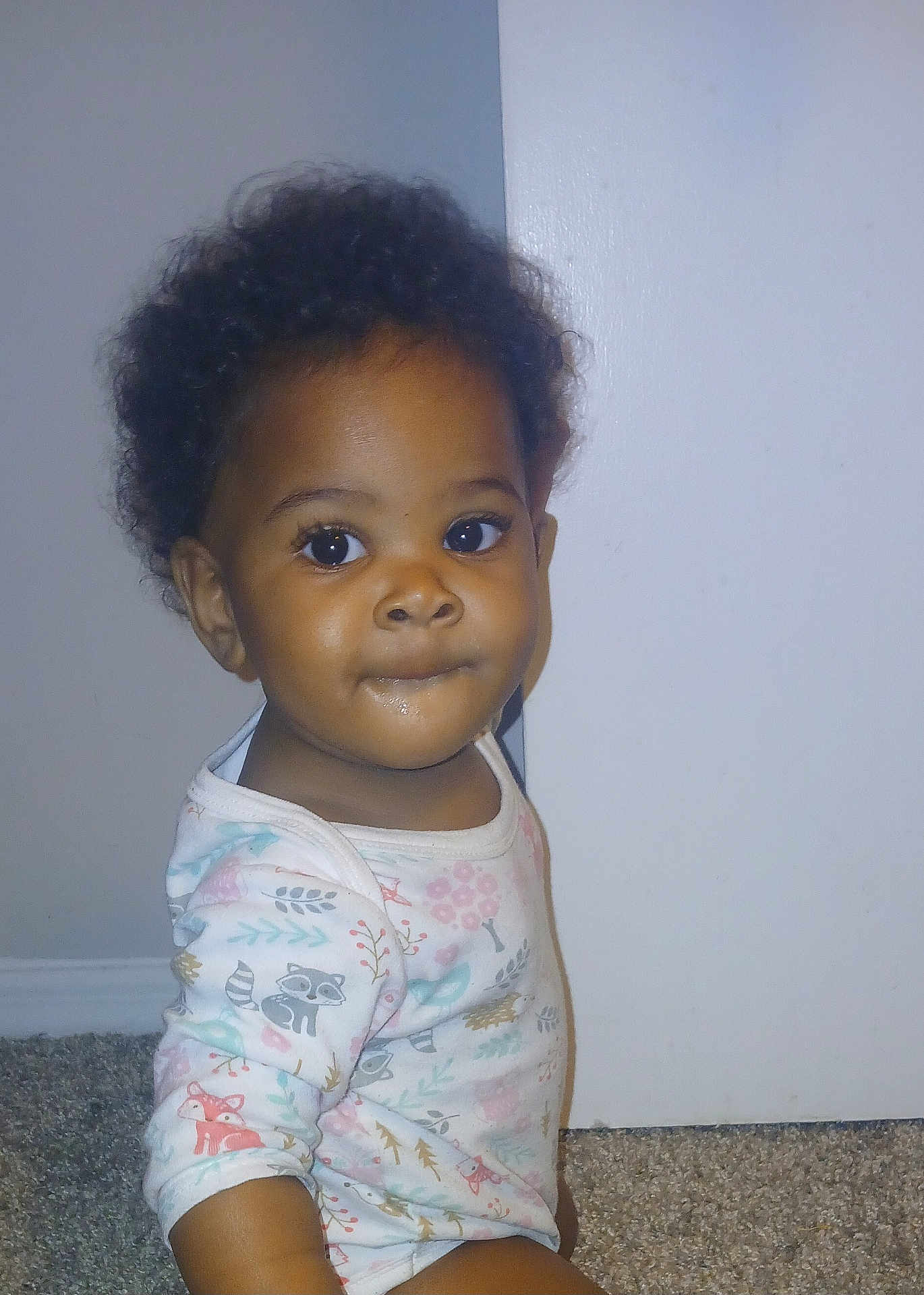 Elaya is registered to the contest to win money with this photo: toddler, child, baby, onesie, indoor, carpet, curly_hair, face, person, cute, expression, sitting, animal_print, long_sleeve, infant, portrait, young_child, looking, floor, wall