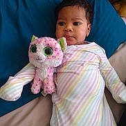 Elaya is registered to the contest to win money with this photo: baby, child, stuffed_animal, plush_toy, bed, blanket, striped_clothing, onesie, indoor, person, cute, infant, lying_down, soft_toy, pink, white, green_eyes, expression, comfort, resting