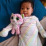 baby, child, stuffed_animal, plush_toy, bed, blanket, striped_clothing, onesie, indoor, person, cute, infant, lying_down, soft_toy, pink, white, green_eyes, expression, comfort, resting