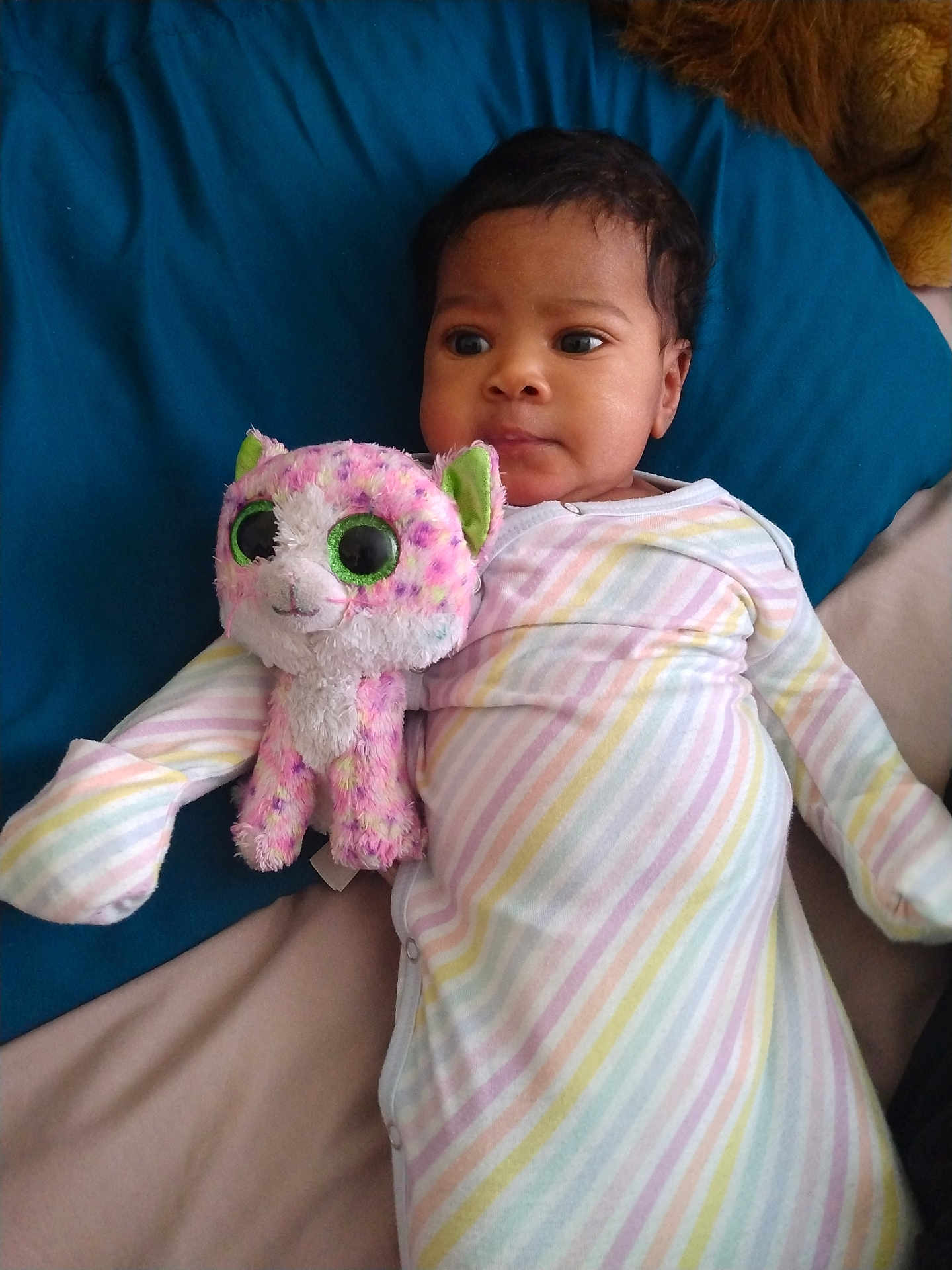 Elaya is registered to the contest to win money with this photo: baby, child, stuffed_animal, plush_toy, bed, blanket, striped_clothing, onesie, indoor, person, cute, infant, lying_down, soft_toy, pink, white, green_eyes, expression, comfort, resting