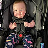 baby, car_seat, child, dinosaur_pants, infant, seat_belt, smile, cute, socks, clothing, straps, happy, young_child, indoor, person, safety, head, face, hands, transportation