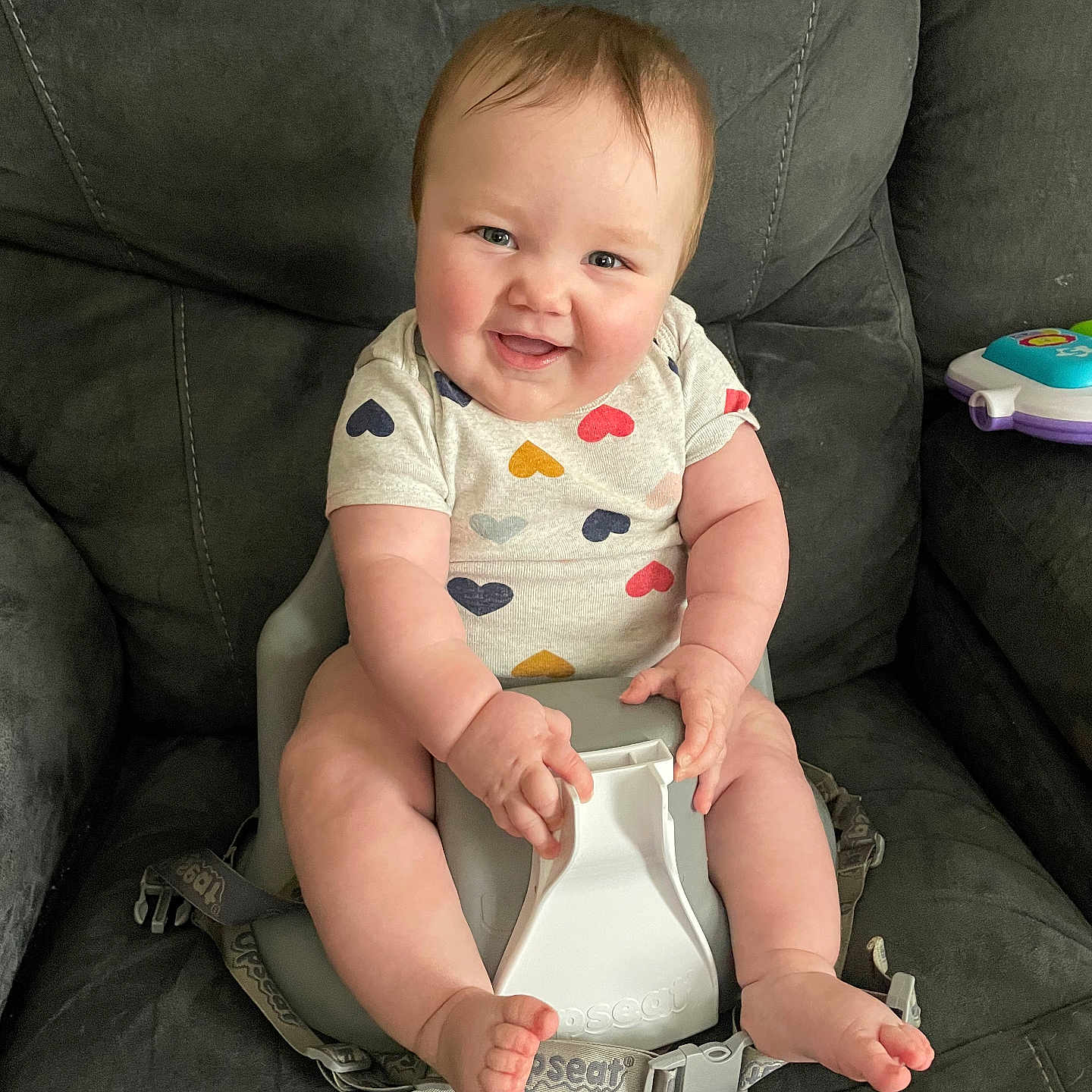Aurelia joined the competition — help win amazing prizes! baby, infant, smiling, heart_pattern, onesie, baby_seat, straps, couch, gray_furniture, happy, cute, chubby, skin, person, indoor, child, seat, foot, hand, face