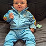 baby, child, blue_tracksuit, adidas, sneakers, pacifier, blanket, soft_fabric, indoor, seated, curious, wide_eyes, casual_clothing, infant, portrait, couch, comfortable, relaxed, fashion, young_child