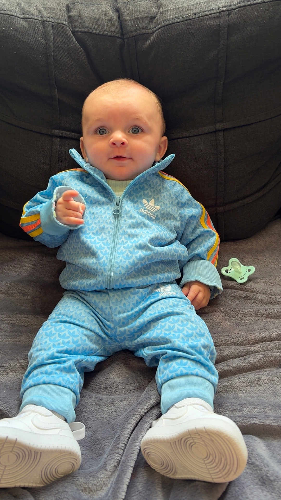 Aylan participe au concours pour gagner de l'argent avec cette photo : baby, child, blue_tracksuit, adidas, sneakers, pacifier, blanket, soft_fabric, indoor, seated, curious, wide_eyes, casual_clothing, infant, portrait, couch, comfortable, relaxed, fashion, young_child