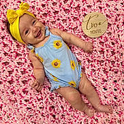 Zoe joined the competition — help win amazing prizes! baby, infant, smiling, yellow_headband, blue_onesie, sunflower_pattern, pink_blanket, wooden_sign, two_months, lying_down, happy, cute, child, portrait, indoors, soft_texture, headwear, clothing, skin, baby_girl