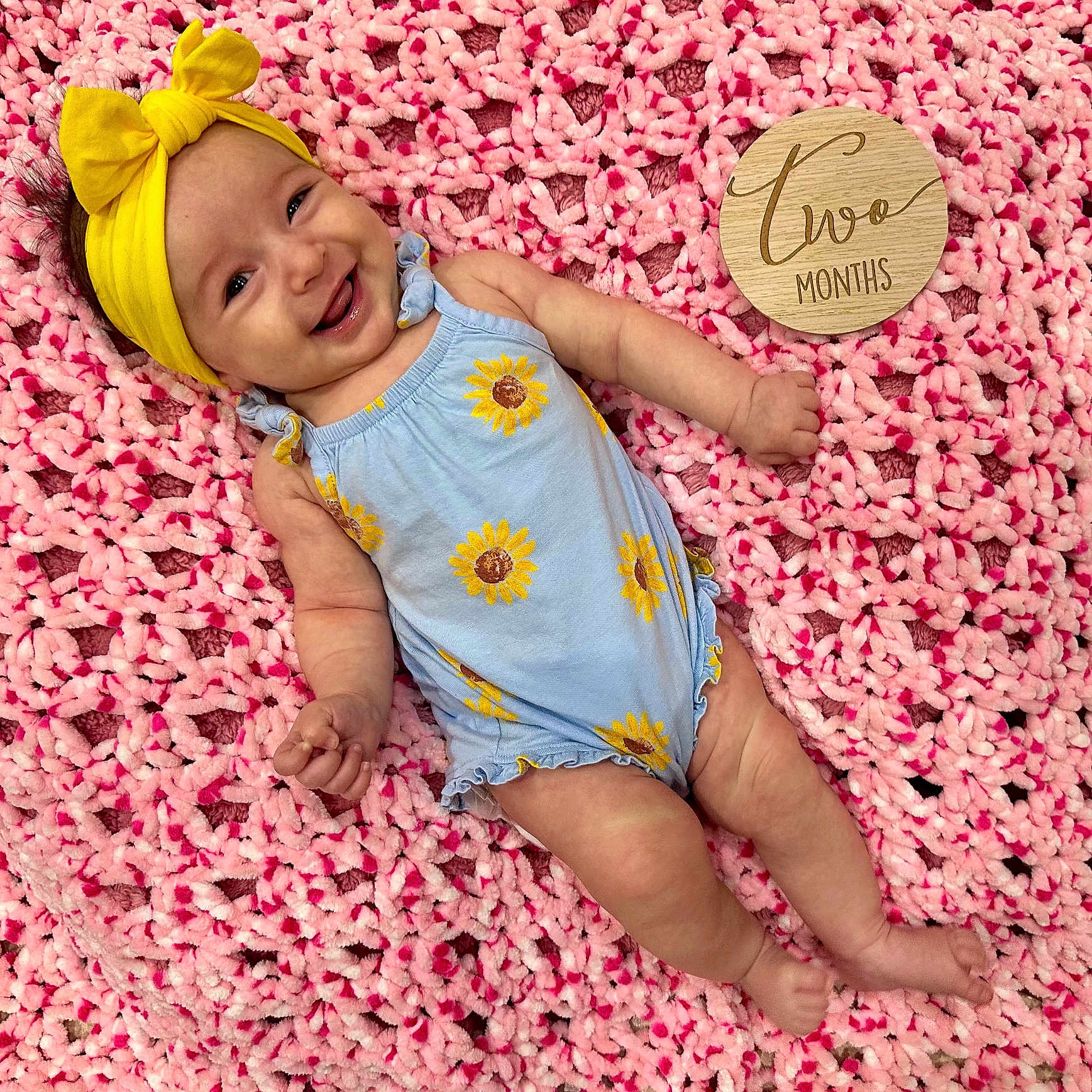 Zoe joined the competition — help win amazing prizes! baby, baby_girl, blue_onesie, child, clothing, cute, happy, headwear, indoors, infant, lying_down, pink_blanket, portrait, skin, smiling, soft_texture, sunflower_pattern, two_months, wooden_sign, yellow_headband