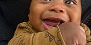 Carter is registered to the contest to win money with this photo: baby, brown_skin, child, closeup, clothing, curly_hair, cute, dinosaur_pattern, expression, fabric, face, fist, hand, happy, infant, joy, portrait, seated, smiling, texture