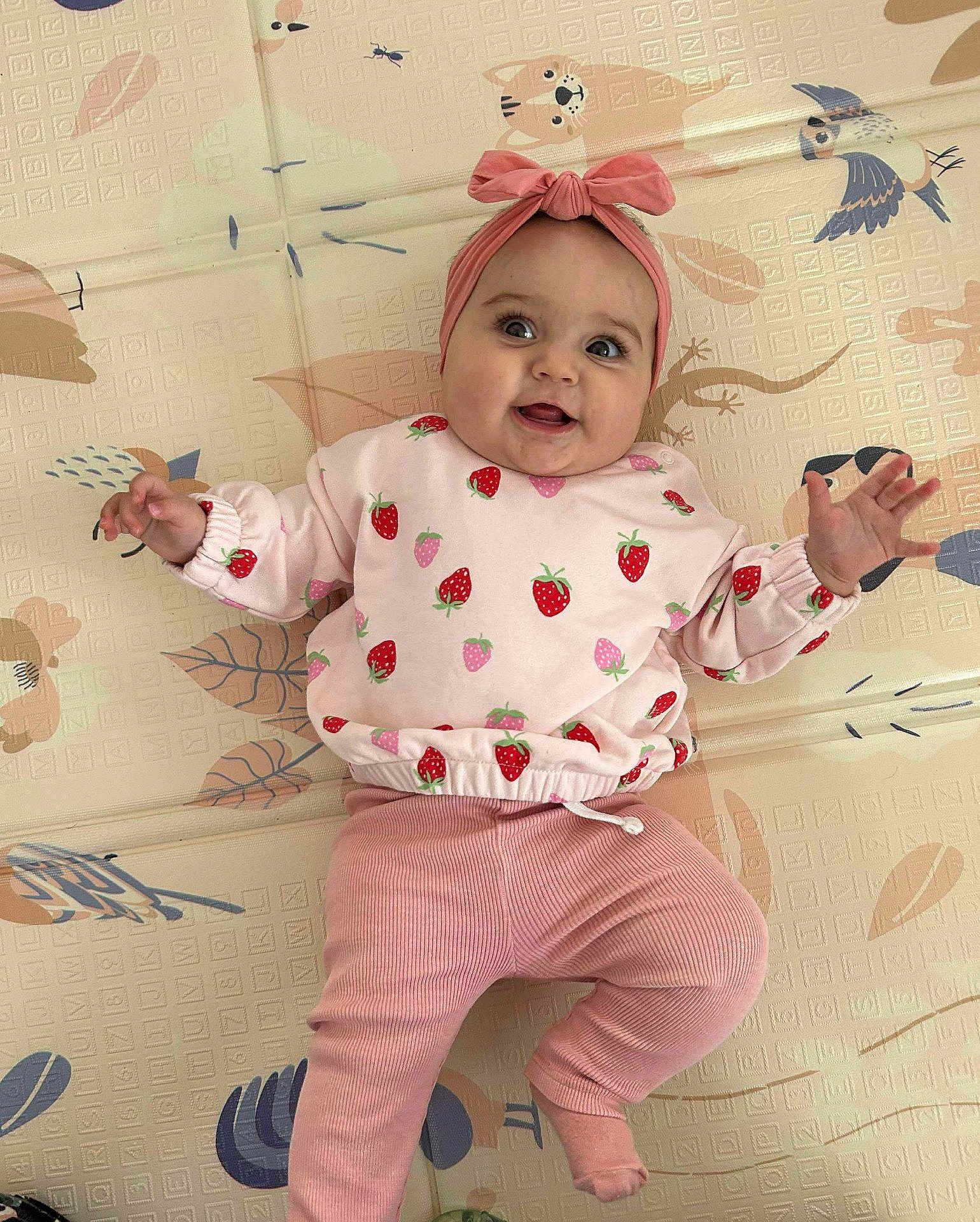 Olivia a rejoint le concours — aidez-le/la à gagner de superbes lots ! baby, child, smiling, pink_clothing, headband, strawberry_pattern, lying_down, playmat, animal_print, cute, happy, infant, toddler, indoor, apparel, expression, portrait, baby_girl, clothing, hand_gesture