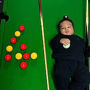 Kendrick a rejoint le concours — aidez-le/la à gagner de superbes lots ! 8_ball, baby, balanced_object, billiard_balls, black_clothing, casual, child, colorful_balls, cue_ball, curious_expression, funny_pose, game_room, green_felt, indoor, lying_down, playing, pool_cues, pool_table, recreation, sports