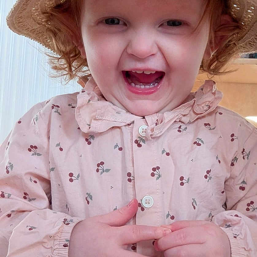 Ondine a rejoint le concours — aidez-le/la à gagner de superbes lots ! buttoned_shirt, cherry_pattern, child, clothing, curly_hair, cute, face, hands, happy, hat, indoor, laughing, person, pink_shirt, portrait, radiant, smiling, straw_hat, toddler, young_child