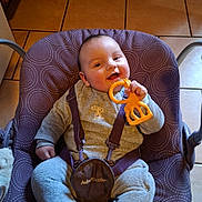 Samuel a rejoint le concours — aidez-le/la à gagner de superbes lots ! baby, infant, baby_seat, teething_toy, giraffe_toy, purple, patterned, straps, clothing, smiling, happy, indoors, floor_tiles, wooden_cabinets, child, cute, playful, comfort, seated, person