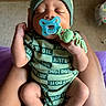 Nikolai joined the competition — help win amazing prizes! baby, infant, sleeping, pacifier, beanie, onesie, clothing, arms, portrait, close_up, indoor, home, adult, hands, legs, green, sitting, calm, cute, textured_fabric