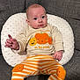 baby, child, clothing, couch, cute, expression, gray_fabric, hand, indoors, infant, knit, orange, person, pillow, portrait, pumpkin, sitting, smiling_pumpkin, striped_pants, sweater