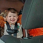 Ocean is registered to the contest to win money with this photo: child, toddler, smile, smiling, car_seat, harness, seatbelt, headrest, vehicle_interior, rear_seat, orange_shirt, camo, hair, face, happy, portrait, seat, upholstery, child_safety, grin