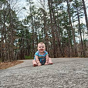 Mahala Logan is registered to the contest to win money with this photo: baby, child, infant, sitting, pavement, path, forest, pine_trees, trees, outdoors, nature, smile, happy, striped_clothing, bare_feet, portrait, ground_texture, sky, woodland, young_child