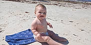 Mahala Logan is registered to the contest to win money with this photo: baby, infant, beach, sand, ocean, towel, diaper, smile, sitting, sunny, seaside, shore, water, wave, barefoot, chubby, horizon, adult, blue_towel, seaweed
