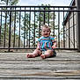 baby, child, smile, sitting, wooden_deck, railing, outdoor, trees, sky, porch, striped_dress, diaper, bare_feet, face, happy, candid, daylight, building, nature, portrait