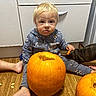 child, baby, pumpkin, floor, carving, seeds, onesie, cartoon, tool, cabinet, wooden_floor, messy_face, indoor, sitting, cute, family_activity, orange, legs, hoodie, playful