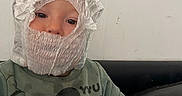 Jordan Junior is registered to the contest to win money with this photo: toddler, child, diaper, face, sweatshirt, mickey_mouse, green_clothing, sitting, couch, hand, indoor, wall, curious, playful, headwear, person, cute, young_child, portrait, casual