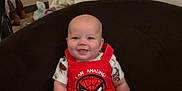 Carson is registered to the contest to win money with this photo: baby, infant, smiling, red_clothing, spiderman, sitting, couch, indoor, child, happy, cute, person, footwear, clothes, wall, home, casual, furniture, light, portrait