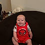 baby, infant, smiling, red_clothing, spiderman, sitting, couch, indoor, child, happy, cute, person, footwear, clothes, wall, home, casual, furniture, light, portrait